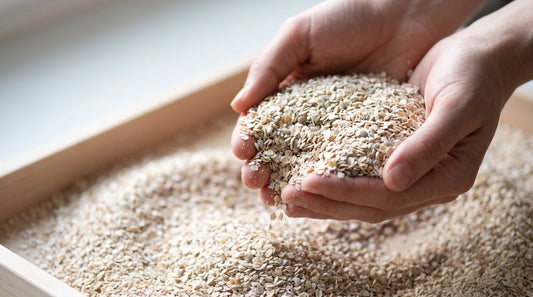 Hands holding cold-processed rye bran above a timber tray, showing its pale flaky texture